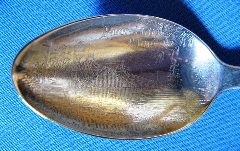 River Hill Mine Placerville, CA bowl closeup.JPG - SOUVENIR MINING SPOON RIVER HILL MINE PLACERVILLE CALIFORNIA - Sterling silver souvenir spoon, lightly engraved in bowl above engraved depiction of mine and structures RIVER HILL MINE and below PLACERVILLE, CAL., handle finial has California golden bear image with a helical screw shaped handle, sterling mark on reverse, 5 7/8 in. long, 21.9 grams (Placerville is the county seat of California’s El Dorado County.  The town played a key role as the central hub for the Mother Lode region’s mining operations.  After the discovery of gold by James W. Marshall in 1848 in nearby Coloma, California some eight miles north of Placerville, the small town of Placerville was known as Dry Diggins after the manner in which the miners moved cartloads of dry soil to running water to separate the gold from the soil. With the Gold Rush riches came problems and later in 1849, the town earned its more common historical name, Hangtown, because of the numerous hangings that occurred there.  In 1854 the town’s name was changed to a friendlier-sounding Placerville and the town was incorporated.  At the time of incorporation, Placerville was the third largest city in California, a testament to the town’s importance to the development of the Mother Lode with its many services, transportation of goods and people, lodging, banking, market and general store.  The Placerville District includes the placer deposits here and in the adjacent Smith Flat, Diamond Springs, Texas Hill, Coon Hollow, and White Rock areas as well as the lode mines of the Mother Lode belt.  The lode-gold deposits are massive quartz veins as much as 20 feet thick with numerous parallel stringers. The ore bodies are low to moderate in grade (1/7 to 1/4 ounce of gold per ton), but the veins have been mined to depths of 2000 feet. The ore contains finely disseminated free gold and small amounts of pyrite. The veins occur chiefly in slate.  The River Hill group of mines, which included the Bell, Gentle Annie, Ball Consolidated, Lucky Star, Lyon and New Era, was located on 178 acres of the Mother Lode, one and one-half miles northwest of Placerville.  Originally worked around 1865 and then from 1890 to 1906, these mines were very rich, and produced quite a large amount of gold. Five parallel veins, with ore shoots up to twenty feet in width and 150 feet in length, were developed by 1550-foot and 600-foot inclined shafts, a 2400-foot adit and much drifting. The ore was originally treated in a ten-stamp mill, which was replaced with a twenty-stamp mill in 1901. The Placerville lode mining operations pretty much ceased activity by about 1915.)